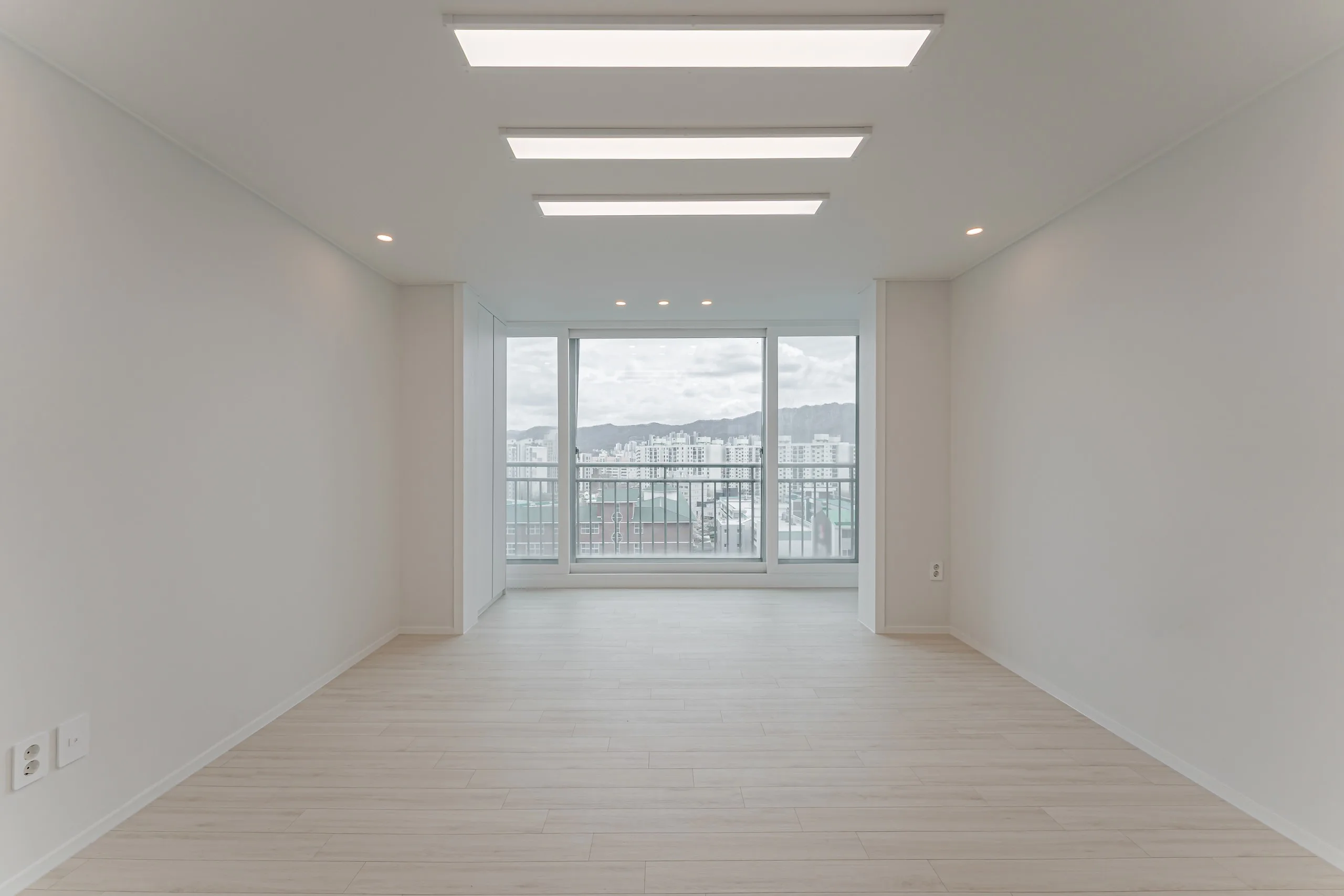 가락쌍용1차 24평 거실. 세 줄 조명 아래 밝은 마루가 창가까지 이어지고 창밖으로 산이 보인다